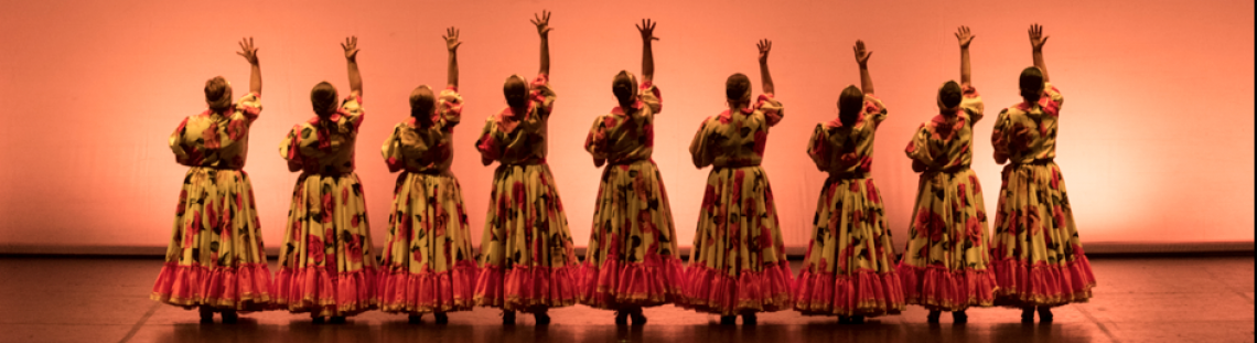 Mujeres  danzando en el escenario con trajes coloridos.