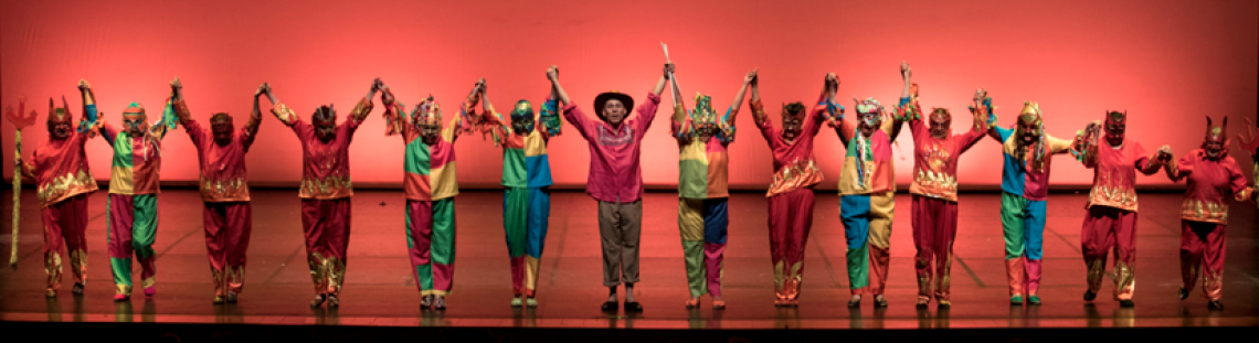 Personas en el escenario con trajes coloridos y brazos en alto