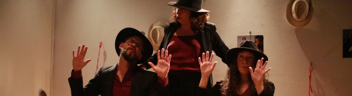 Dos mujeres y un hombre con sombreros y las manos arriba