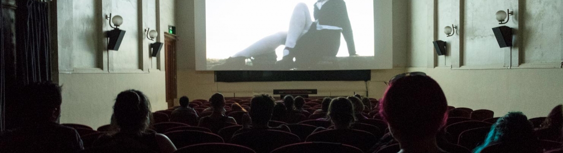 Personas en una sala de cine con una proyección de una mujer en blanco y negro. 