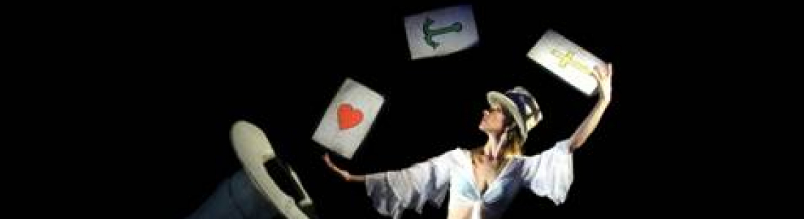Mujer en escena vestida de blanco jugando con cartas gigantes y sombrero