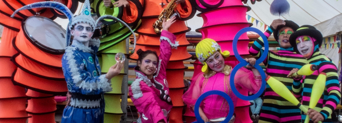 Malabaristas y zanqueros vestidos en colores vivos debajo de una carpa de día