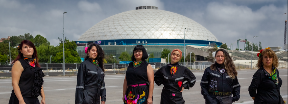 Seis mujeres vestidas de negro con bordados posando en exterior de día.