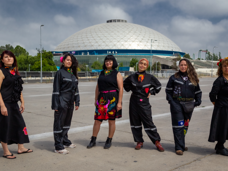 Seis mujeres vestidas con prendas negras y bordadas posando de pie de día.