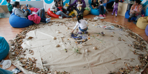 Sala de juegos con niños y madres participando en una actividad