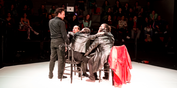 Cuatro actores que hacen parte de una escena de teatro con público al fondo