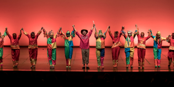 Personas en el escenario con trajes coloridos y brazos en alto