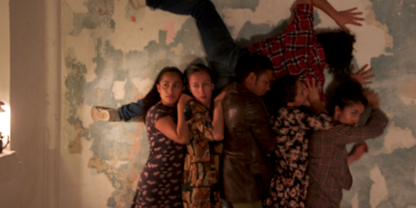 Actores sosteniendo en alto un cuerpo contra una pared.