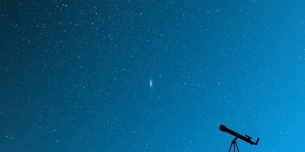 Cielo azul con estrellas y un telescopio en el suelo. 