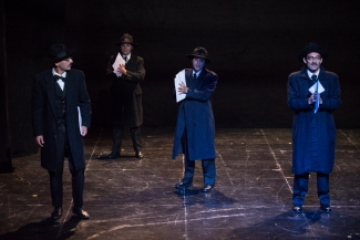 Cuatro actores de negro y sacoleva, sosteniendo papeles en el escenario
