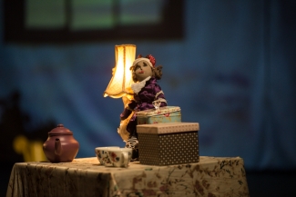 Muñeca con lámpara, cajas y juego de te sobre una mesa