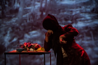 Actriz sin rostro y abrigo rojo inclinada sobre una mesa llena de cosas