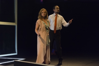 Hombre  con traje de corbata y mujer con bata hablando en el escenario