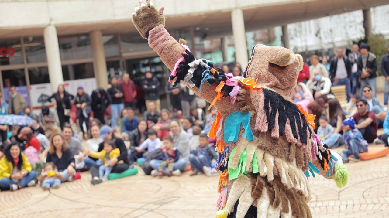 Personaje de con traje de colores en presentación frente a niñas, niños y sus familias