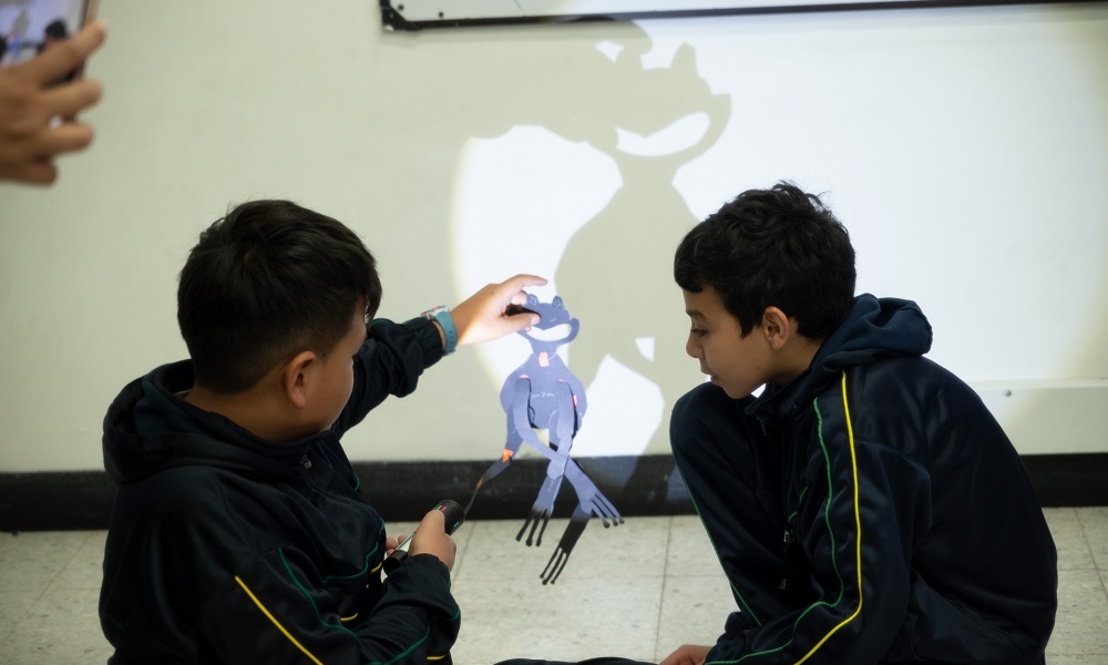 Dos menores de edad juegan con las sombras que hace una figura de papel.