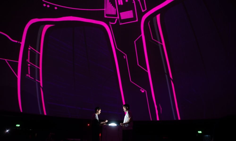 En el domo del planetario dos personas manipulan un dispositivo que les permite cambiar en tiempo real las imagenes y sonidos que se proyectan