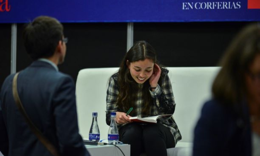 Nuevo premio para la poesía en Bogotá Mujer lee libro en una silla blanca.