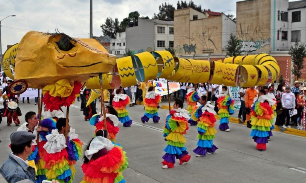 Fotografía: Juan Santacruz. Marcha por la paz. 2013. Comparsa en espacio público, jóvenes danzando con vestidos y una maqueta sobre sus cabezas.