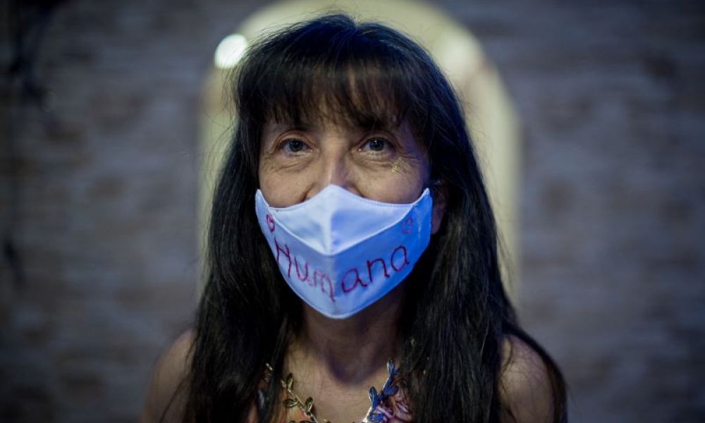 Fotografía: Mathew Valbuena. Mujer mira a la cámara fotográfica con un tapabocas que dice humana.