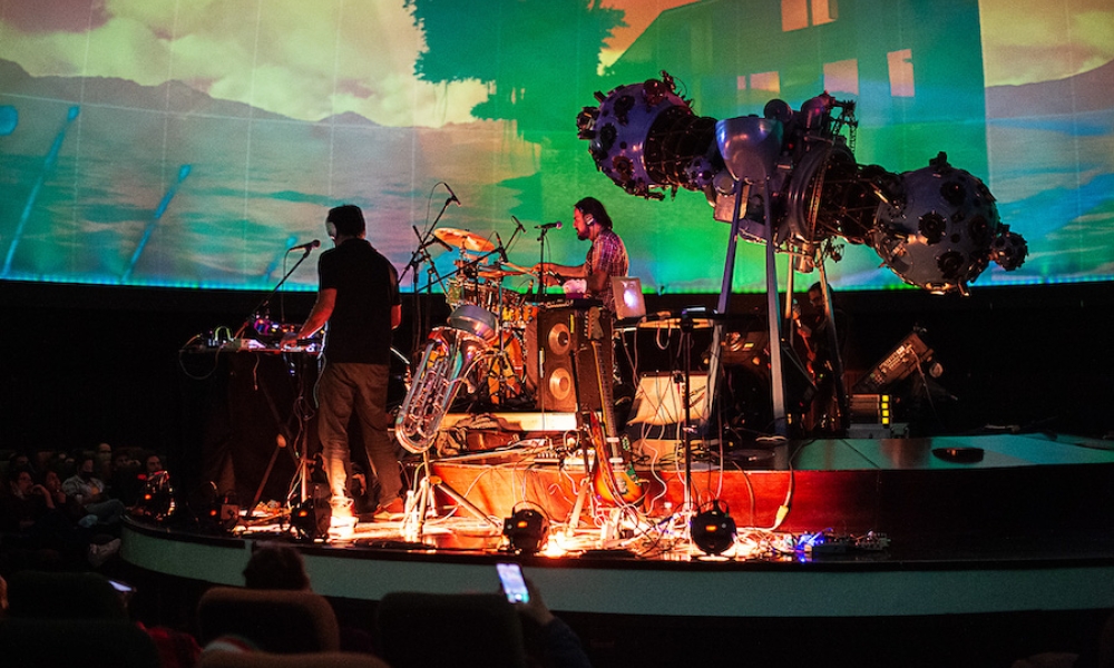 Agrupación musical tocando en vivo en tarima del domo del Planetario de Bogotá con proyección audiovisual. Agrupación musical tocando en vivo en tarima del domo del Planetario de Bogotá con proyección audiovisual.