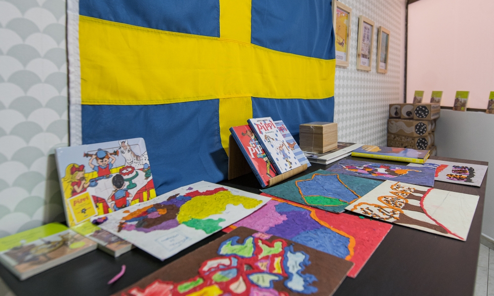 Mesa con libros de Pippi Calzaslargas y obras de arte hechas por niños, en el fondo la bandera de Suecia