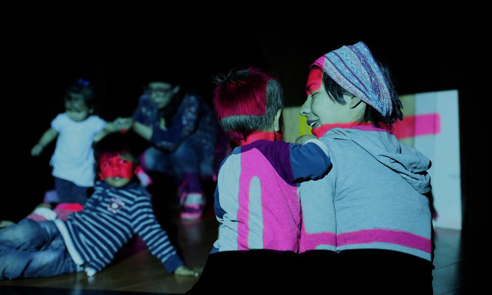 La Toma Dulce para niños y niñas se realizará el 21 de octubre en El Castillo de las Artes. Niños en un cuarto oscuro alumbrados por luces de colores.