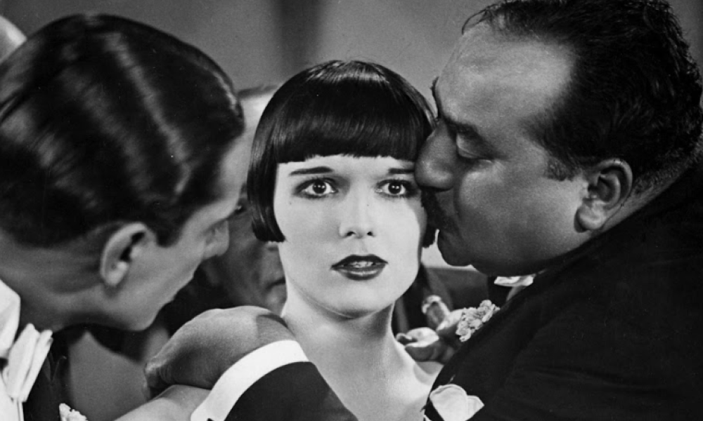 Foto en blanco y negro con dos hombre y una mujer, uno de ellos esta besando la mujer en la mejilla