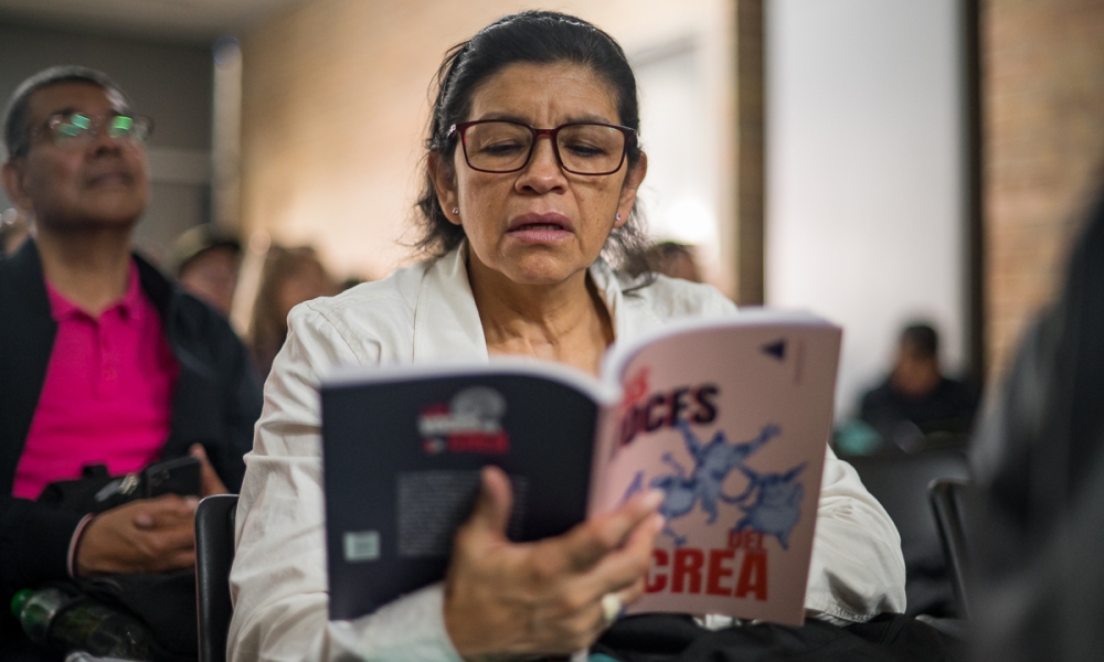Con Las voces del Crea, el Instituto Distrital de las Artes – Idartes presenta toda la riqueza musical del Programa Crea. Durante un evento, una mujer lee un ejemplar del libro Las voces del Crea