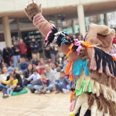 Artista con traje de colores en presentación frente a niños, niñas y sus famlias