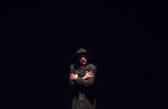 Hombre vestido de negro con telón oscuro y brazos cruzados sobre el pecho