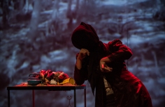 Actriz sin rostro y abrigo rojo inclinada sobre una mesa llena de cosas