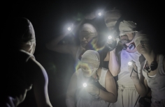 Grupo de actores con los ojos vendados y luces de linterna.