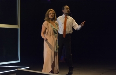 Hombre  con traje de corbata y mujer con bata hablando en el escenario