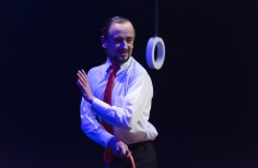 Actor de teatro con camisa y corbata y circulo que cuelga sobre el escenario