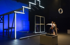 Set teatral con esqueleto de casa y actores espalda con espalda