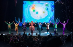 Actores recibiendo aplausos sobre el escenario con fondo de burbujas coloridas