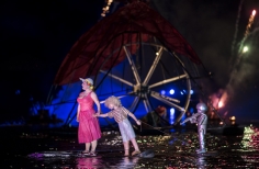Mujer con niño - marioneta sobre el lago iluminado con rueda gigante a la espalda.
