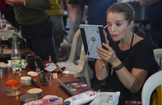 Actriz maquillandose frente a un espejo de mano y maquillaje sobre una mesa.