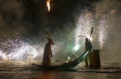 Actir con máscara en góndola sobre lago y muchas luces.