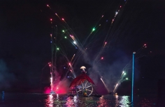 Mujer sobre rueda gigante y luces de colores sobre el lago.