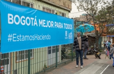 Hombre disfrazado y con sombrilla frente a anuncio de Bogotá Mejor para Todos.