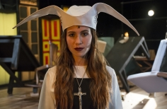 Mujer con sombrero de monja y crucifijo, observando 