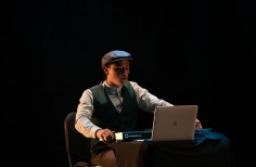 joven sentado frente a una pantalla de computador, una escena teatral