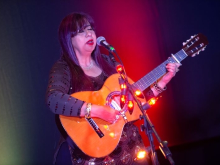 Mujer cantando en el escenario con guitarra en mano