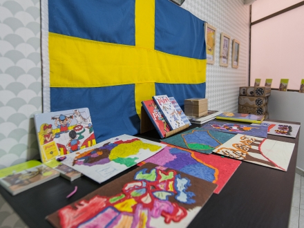 Mesa con libros de Pippi Calzaslargas y obras de arte hechas por niños, en el fondo la bandera de Suecia