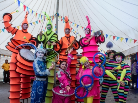 Malabaristas y zanqueros vestidos en colores vivos debajo de una carpa de día