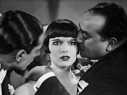 Foto en blanco y negro con dos hombre y una mujer, uno de ellos esta besando la mujer en la mejilla