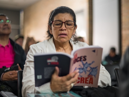 Durante un evento, una mujer lee un ejemplar del libro Las voces del Crea