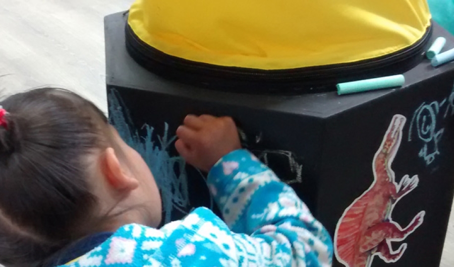 Niña dibujando con tiza de colores un cubo negro de madera.