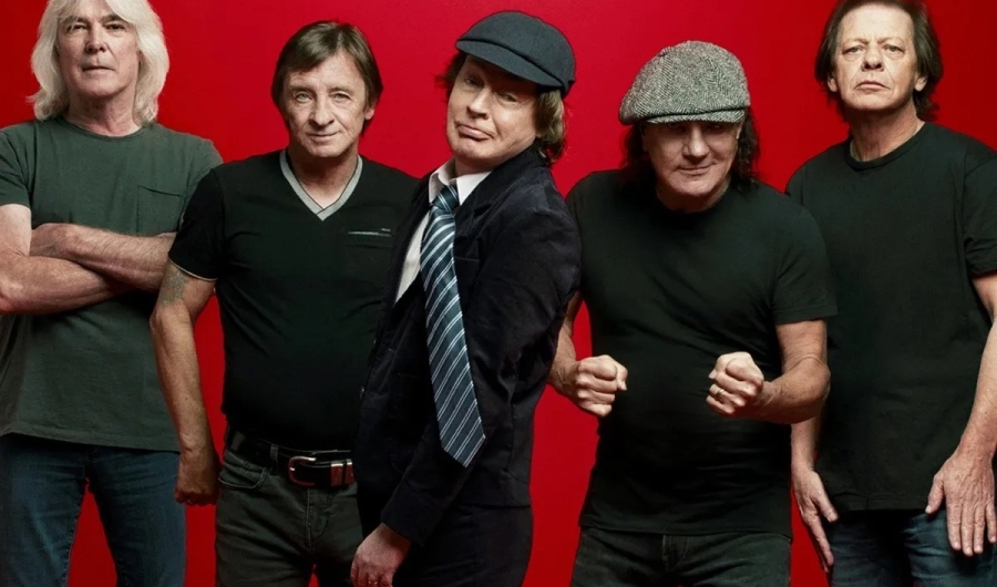 Cinco integrantes de ACDC vestidos de oscuro con fondo rojo.
